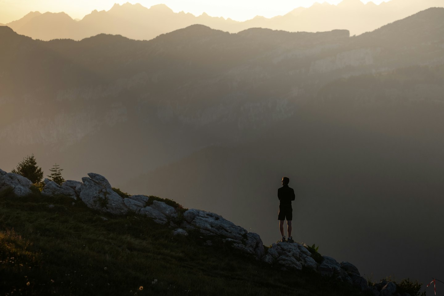 Eine Person steht auf einem Berggipfel und blickt auf entfernte Gebirgszüge.